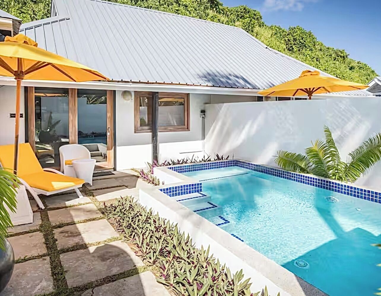 A modern pool area with a clear blue pool, yellow umbrellas, and a white building with large windows.