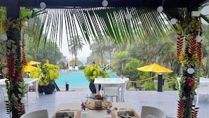 Un espace de restauration en plein air avec vue sur la piscine, entouré de plantes tropicales et de parasols.