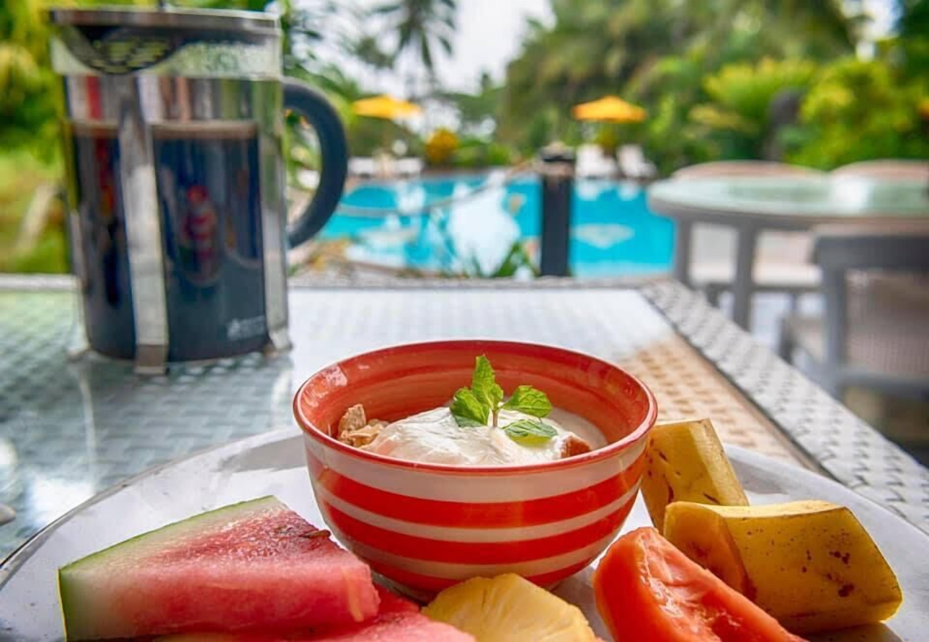 A table with a bowl of yogurt topped with a mint leaf, surrounded by watermelon and pineapple slices.