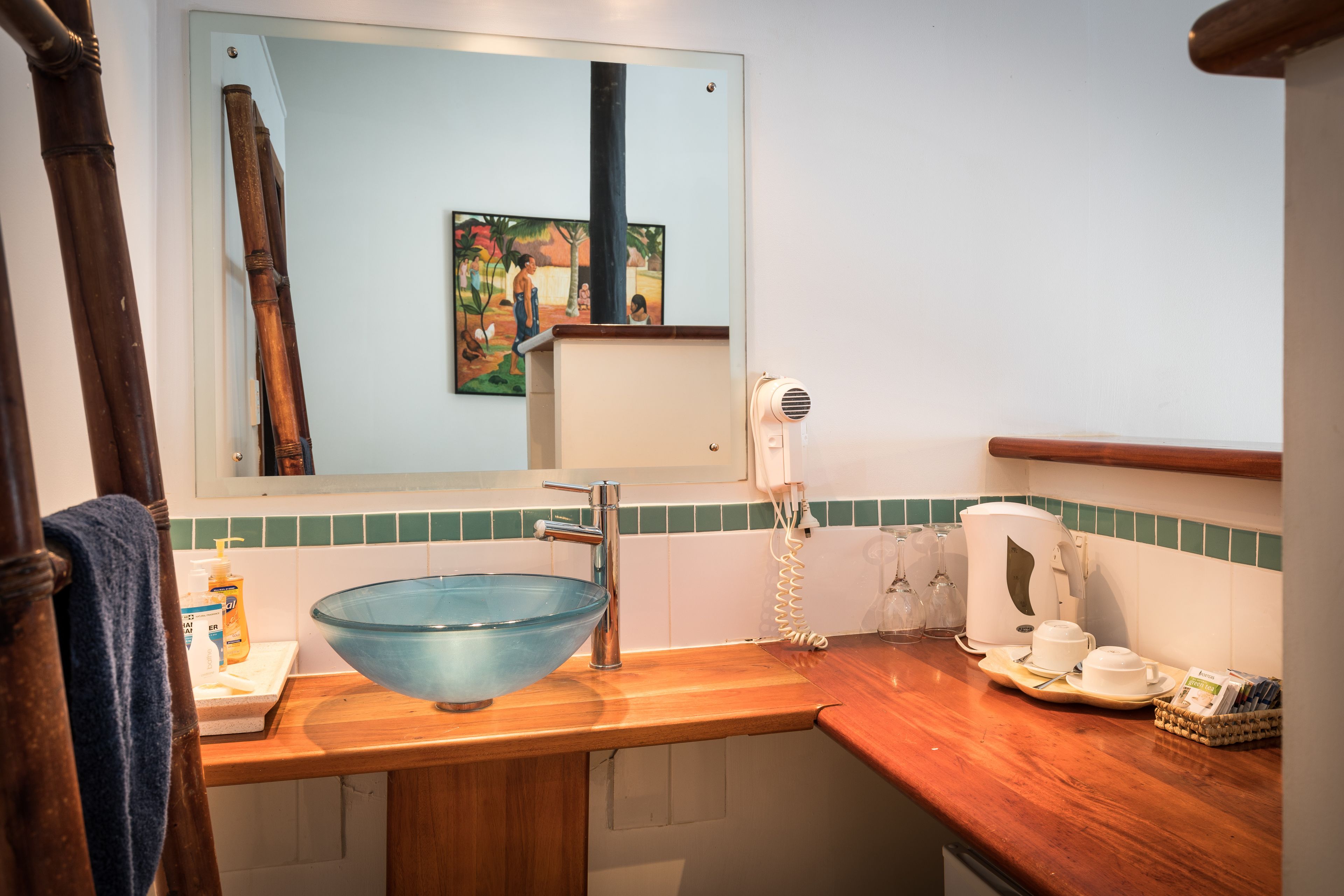 Un baño con encimera de madera, lavabo de vidrio, secador de pelo y un cuadro en la pared.