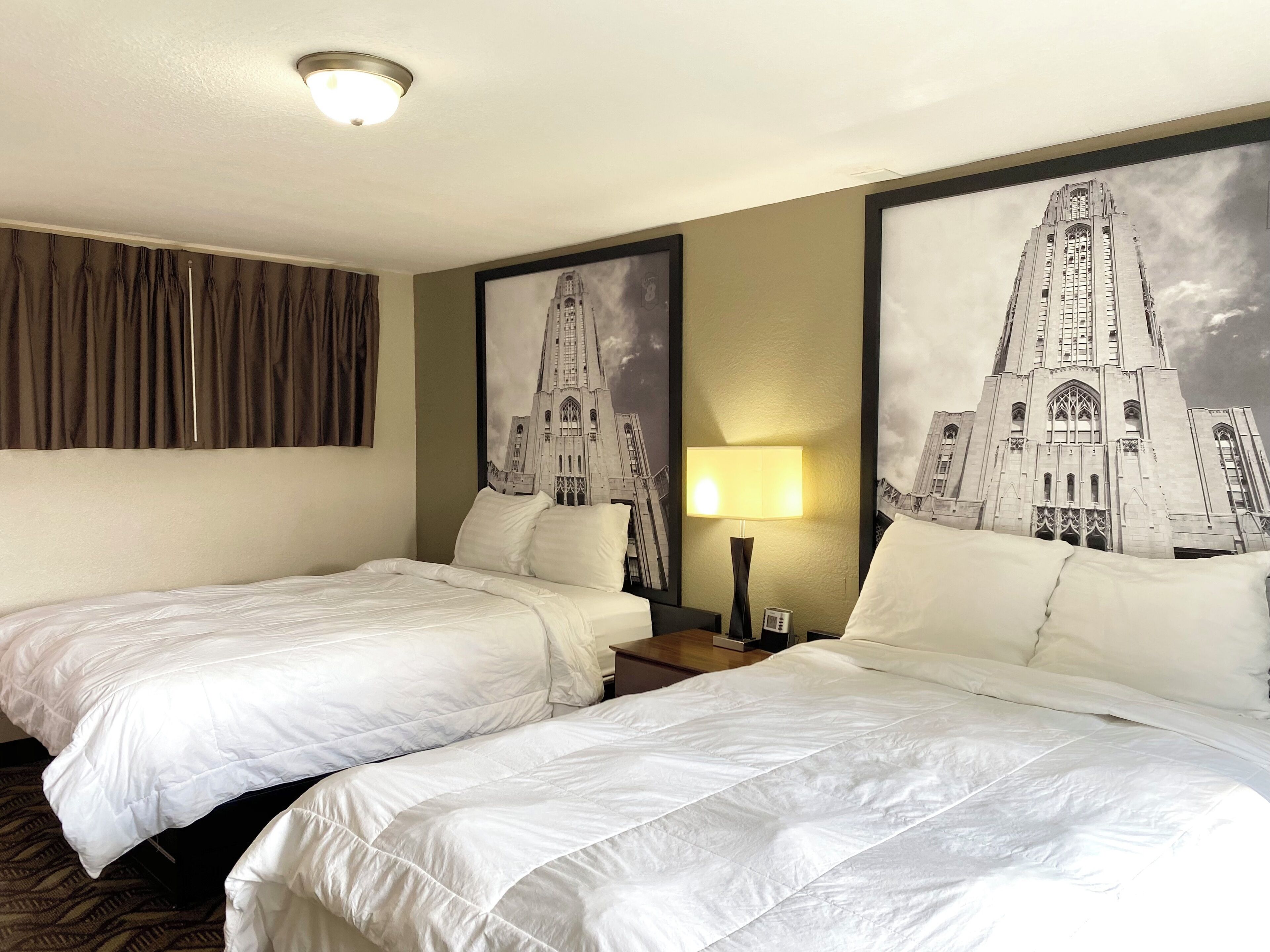 A hotel room with two beds, a nightstand with a lamp, and a large framed picture of a building on the wall.