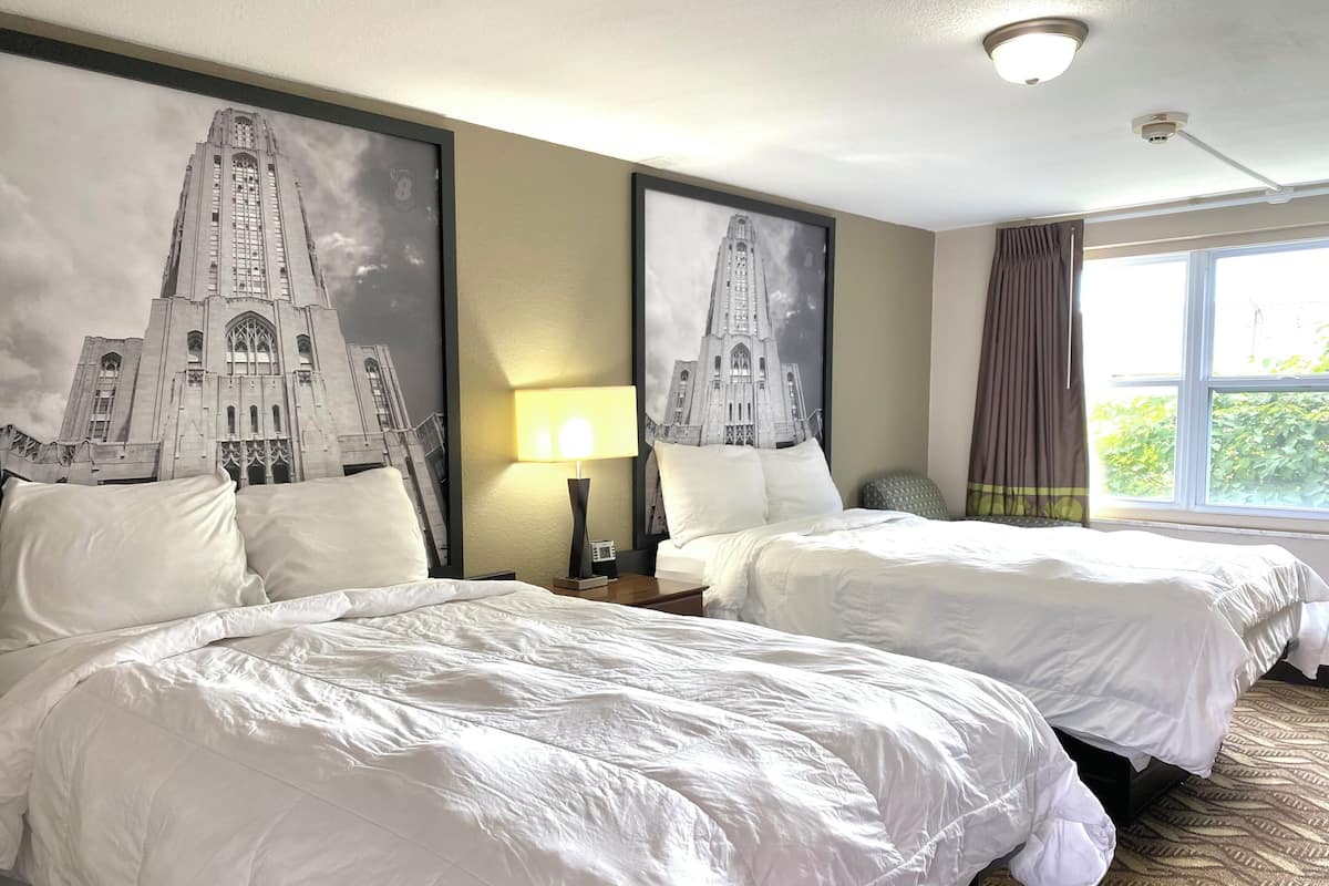 A hotel room with two beds, a large window, and a lamp on the nightstand.