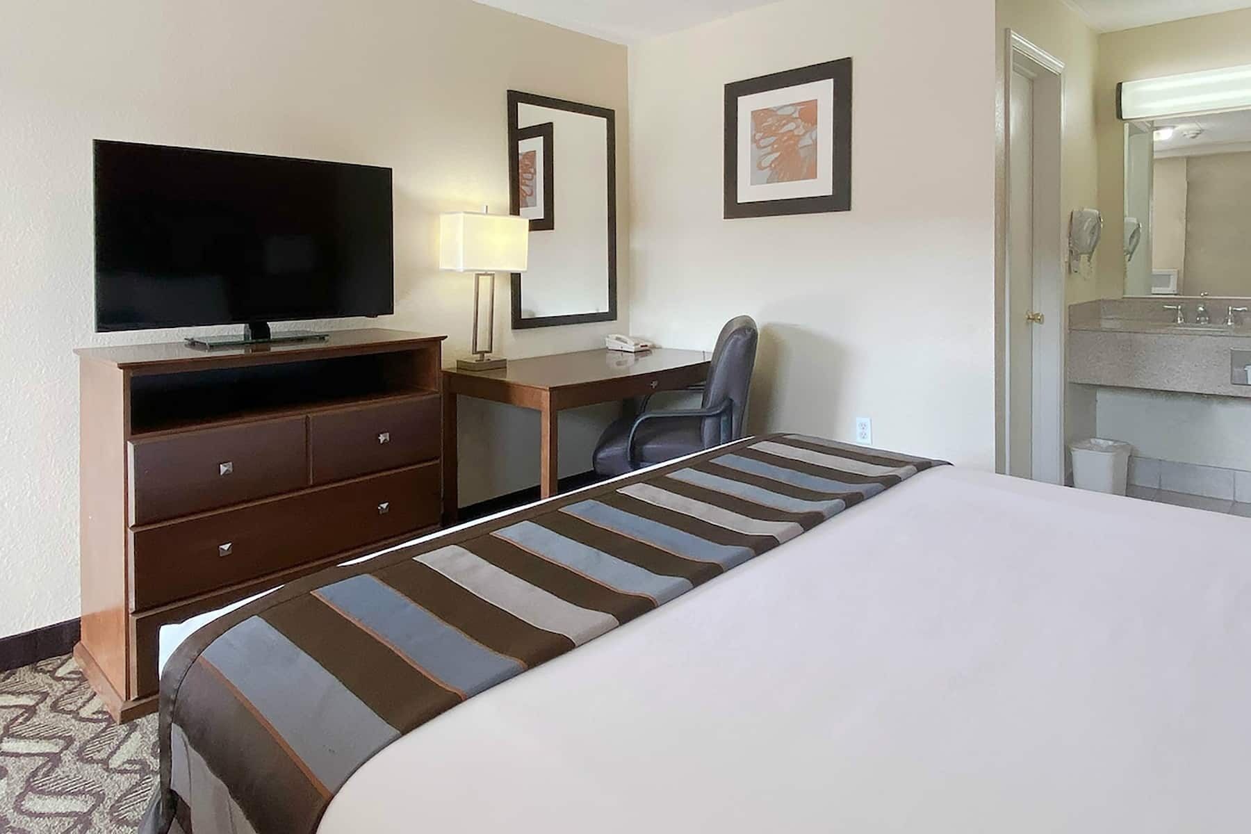 Una camera d'albergo con un letto, una scrivania, una sedia, un televisore e un bagno visibile attraverso una porta aperta.