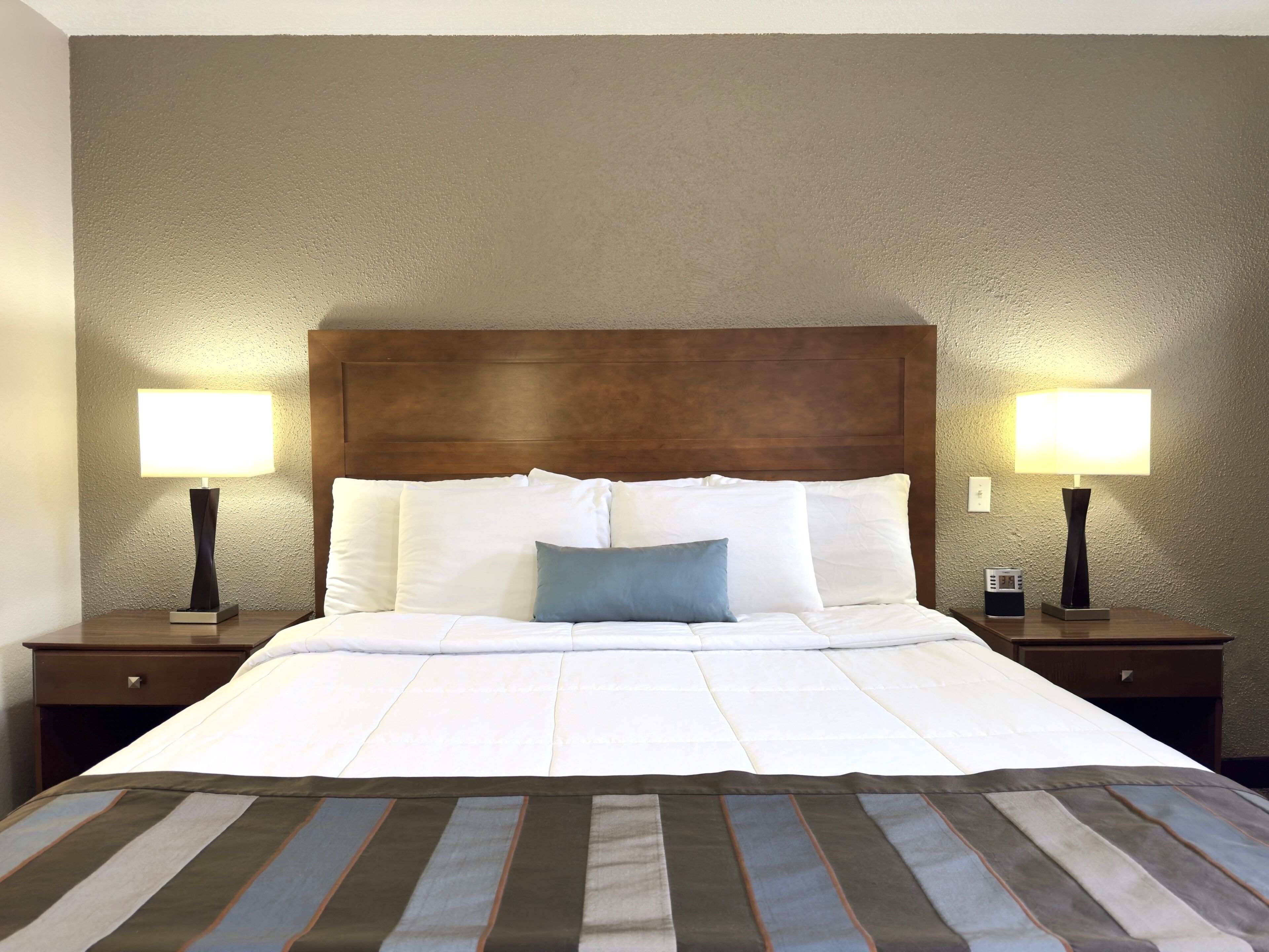 A hotel room with a large bed, two bedside tables, and two wall-mounted lamps.