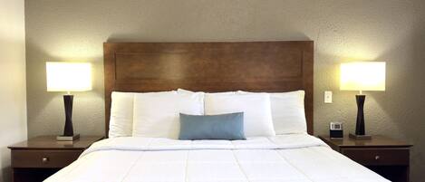 Una habitación de hotel con una cama grande, dos mesitas de noche y dos lámparas fijadas a la pared.