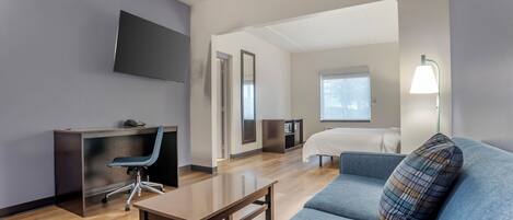 Une chambre d’hôtel moderne équipée d’un bureau, d’une chaise, d’un canapé et d’un téléviseur fixé au mur.
