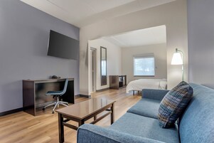 Ein modernes Hotelzimmer mit Schreibtisch, Stuhl, Sofa und Fernseher an der Wand.