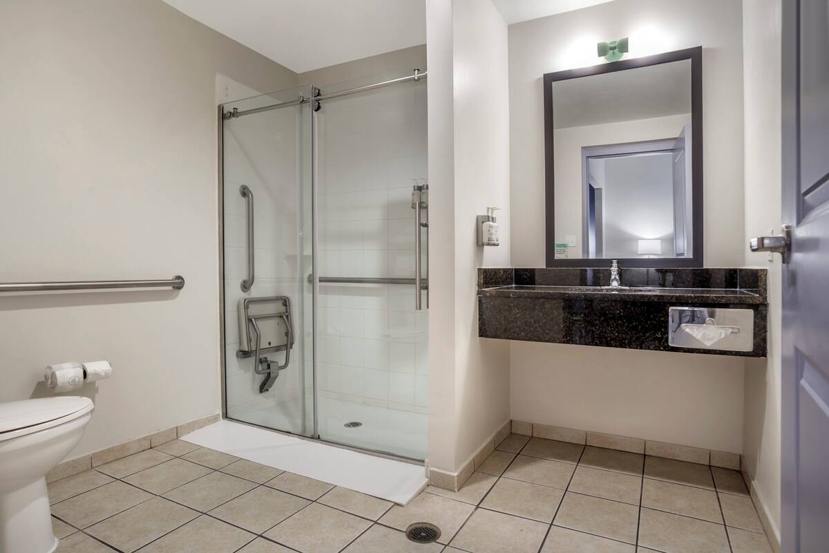 Une salle de bain moderne avec une douche à parois de verre, des toilettes blanches, un lavabo doté d’un plan de travail foncé et un miroir au-dessus du lavabo.