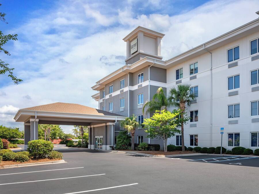 A multi-story hotel with a covered entrance, a parking lot, and surrounding greenery.