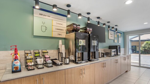 A modern coffee station with a self-serve coffee machine, a variety of coffee creamer options, and a selection of paper cups.