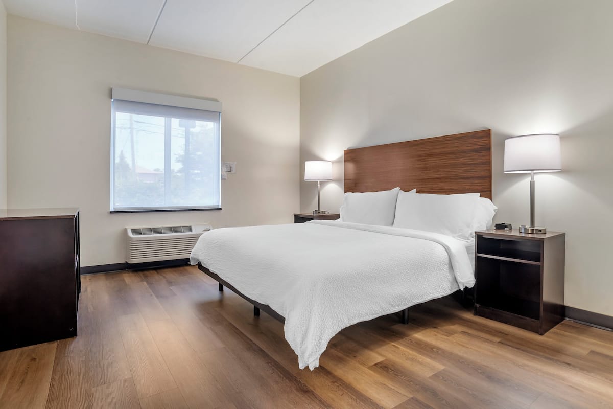 Une chambre d’hôtel avec un grand lit, deux tables de chevet avec des lampes, une fenêtre avec des stores et un radiateur intégré.