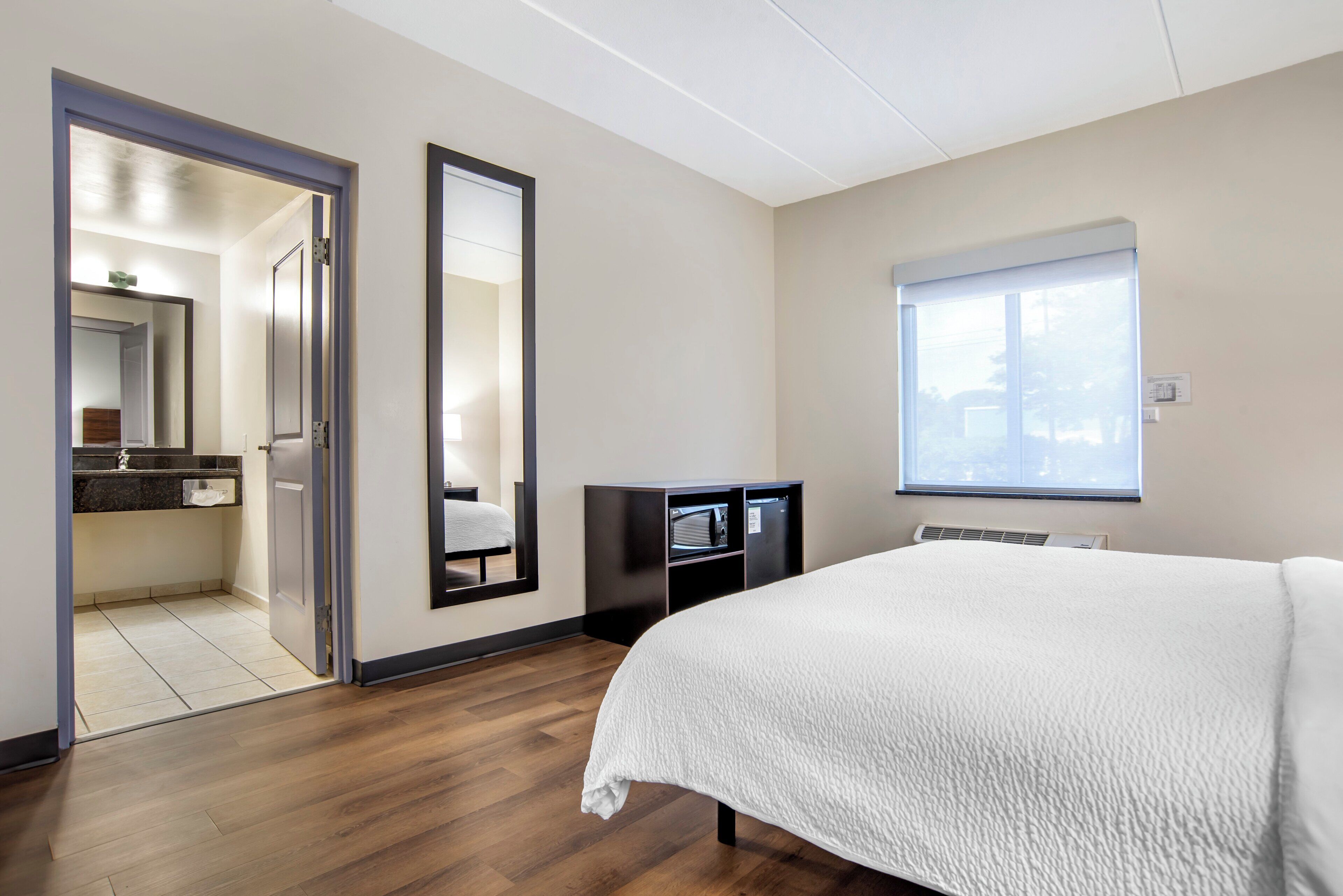 Une chambre d’hôtel avec un grand lit, une armoire, un miroir et une salle de bain visible à travers une porte ouverte.