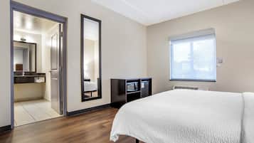Une chambre d’hôtel avec un grand lit, une armoire, un miroir et une salle de bain visible à travers une porte ouverte.