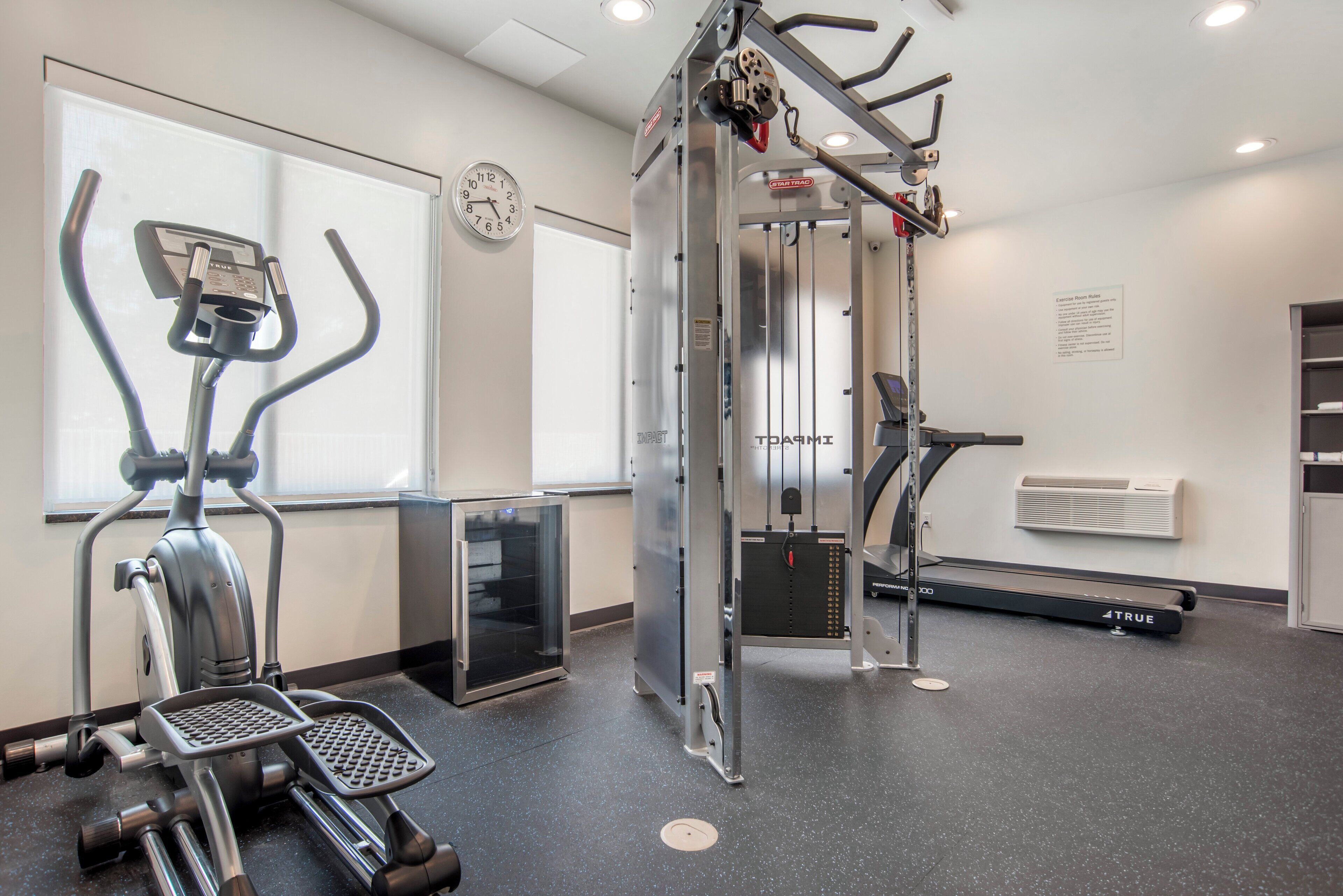 Une salle de sport équipée de matériel d’exercice, avec une horloge et un climatiseur fixé au mur.