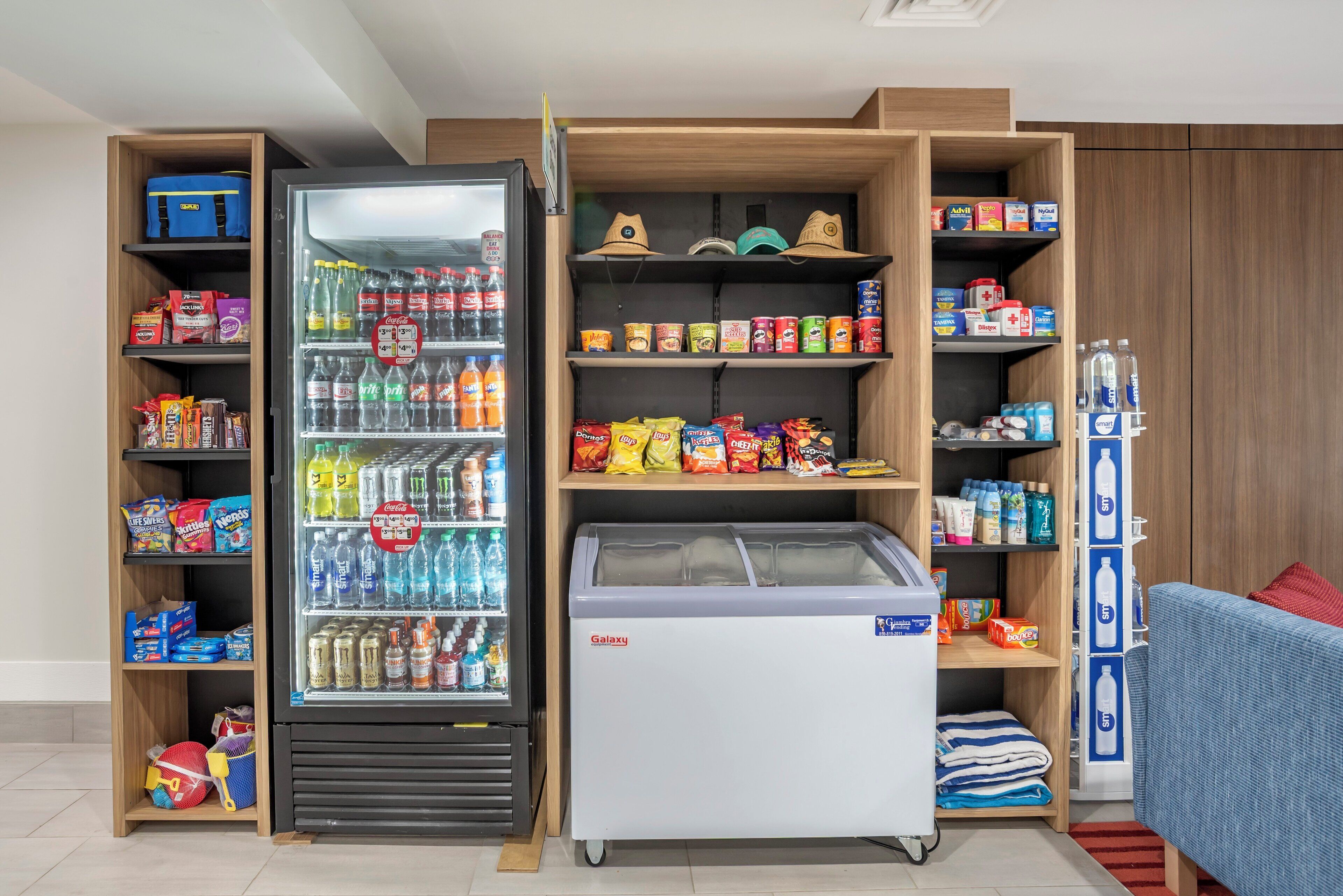 Une chambre d’hôtel équipée d’un mini-bar et de présentoirs remplis de collations, de boissons et d’articles de toilette.