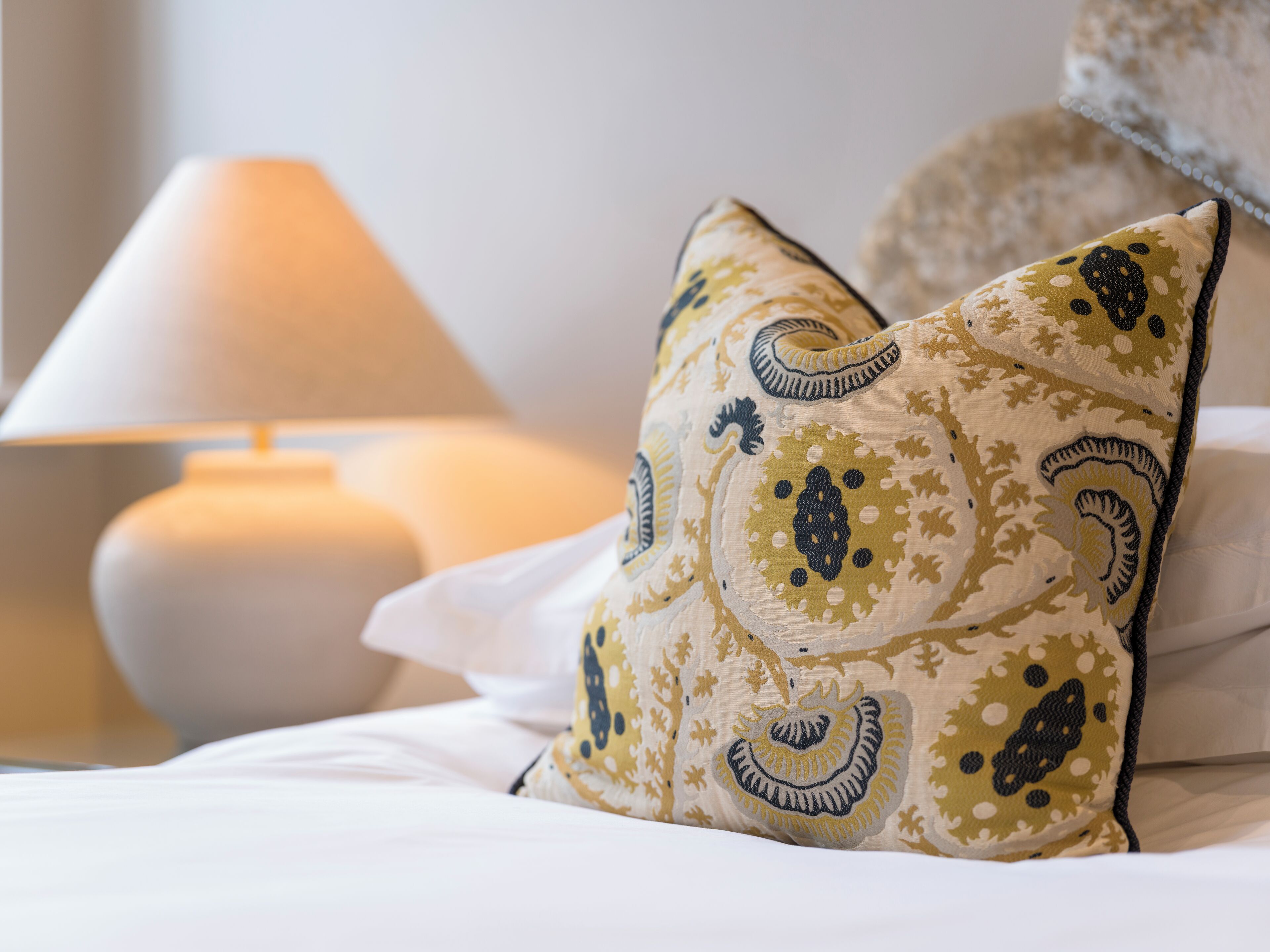 Una cama con sábanas blancas y almohadones decorativos con estampado de cachemir.
