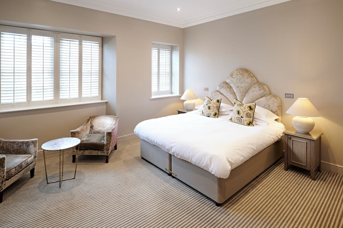 A bedroom with a large bed, two armchairs, a small table, and two bedside lamps.