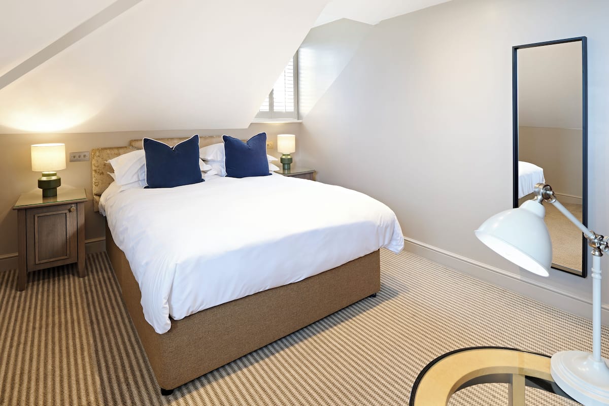 A neatly arranged bedroom with a large bed, two bedside tables with lamps, a mirror, and a patterned carpet.