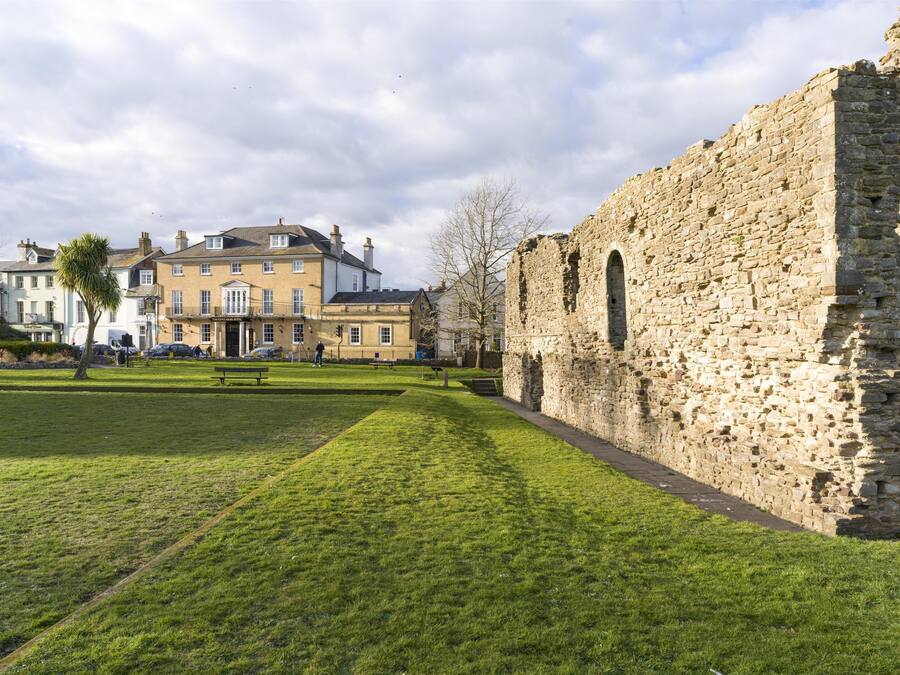 A grassy courtyard with stone ruins and a building with multiple windows.
