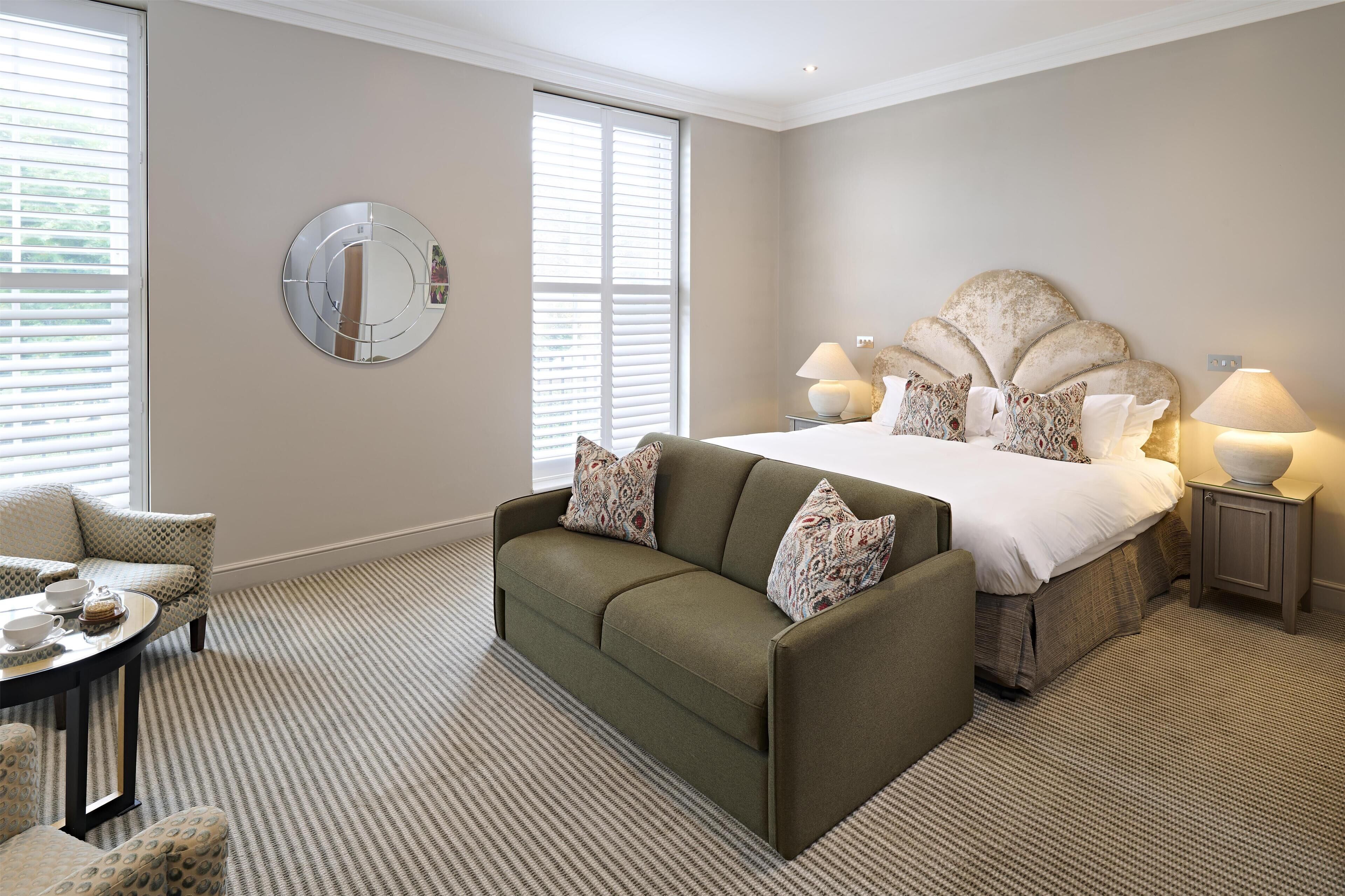 A hotel room with a bed, a sofa, a round mirror, and a small table with a tray.