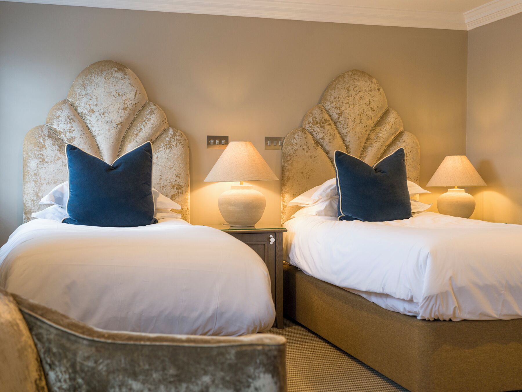 Habitación de hotel con dos camas, cada una con cabecera, lámparas de noche y almohadas.