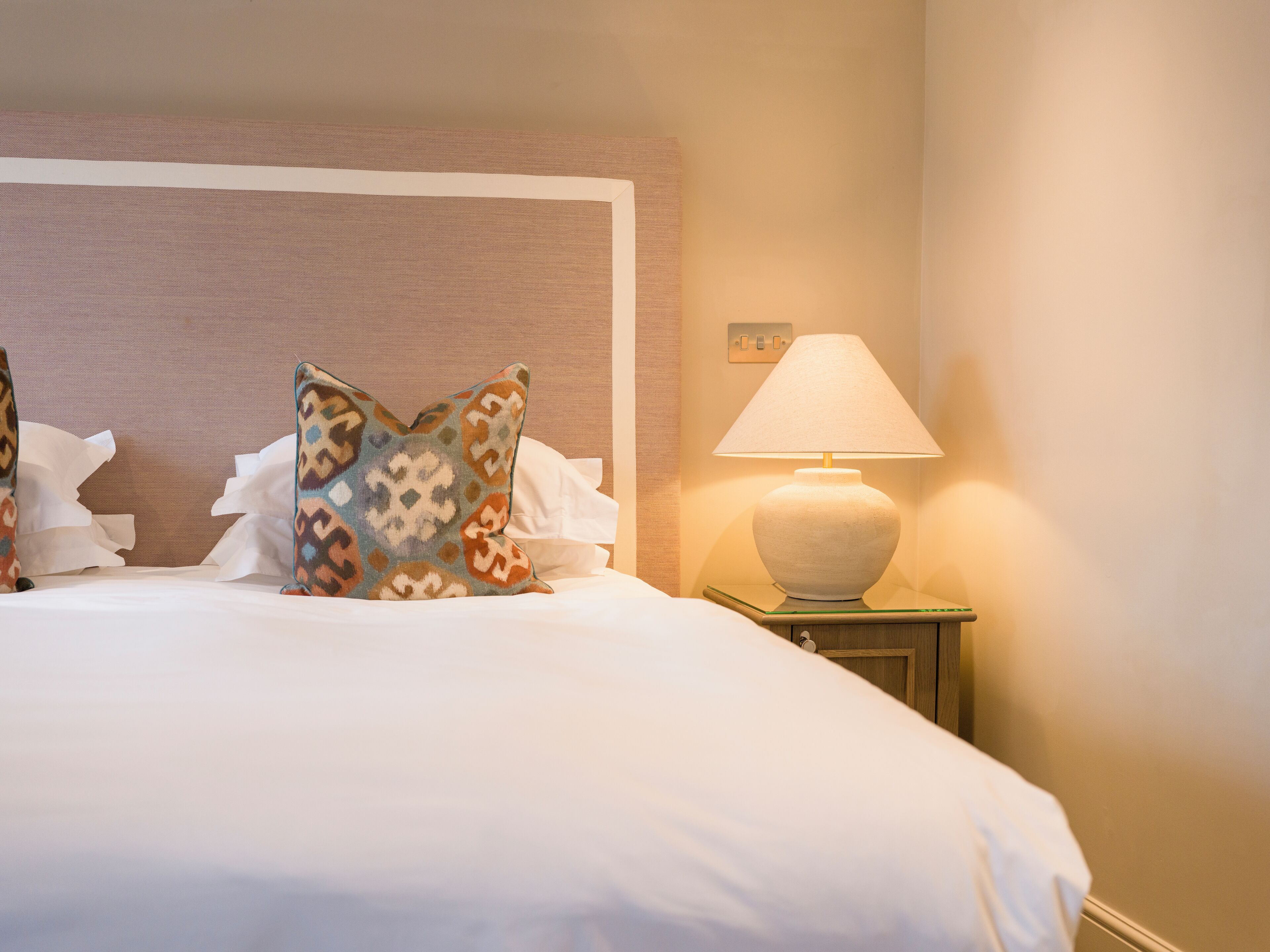 A neatly made bed with patterned pillows, a bedside lamp, and a nightstand.