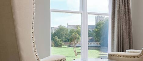 A room with two upholstered chairs and a small round table, a large window with a view of a building and greenery outside.
