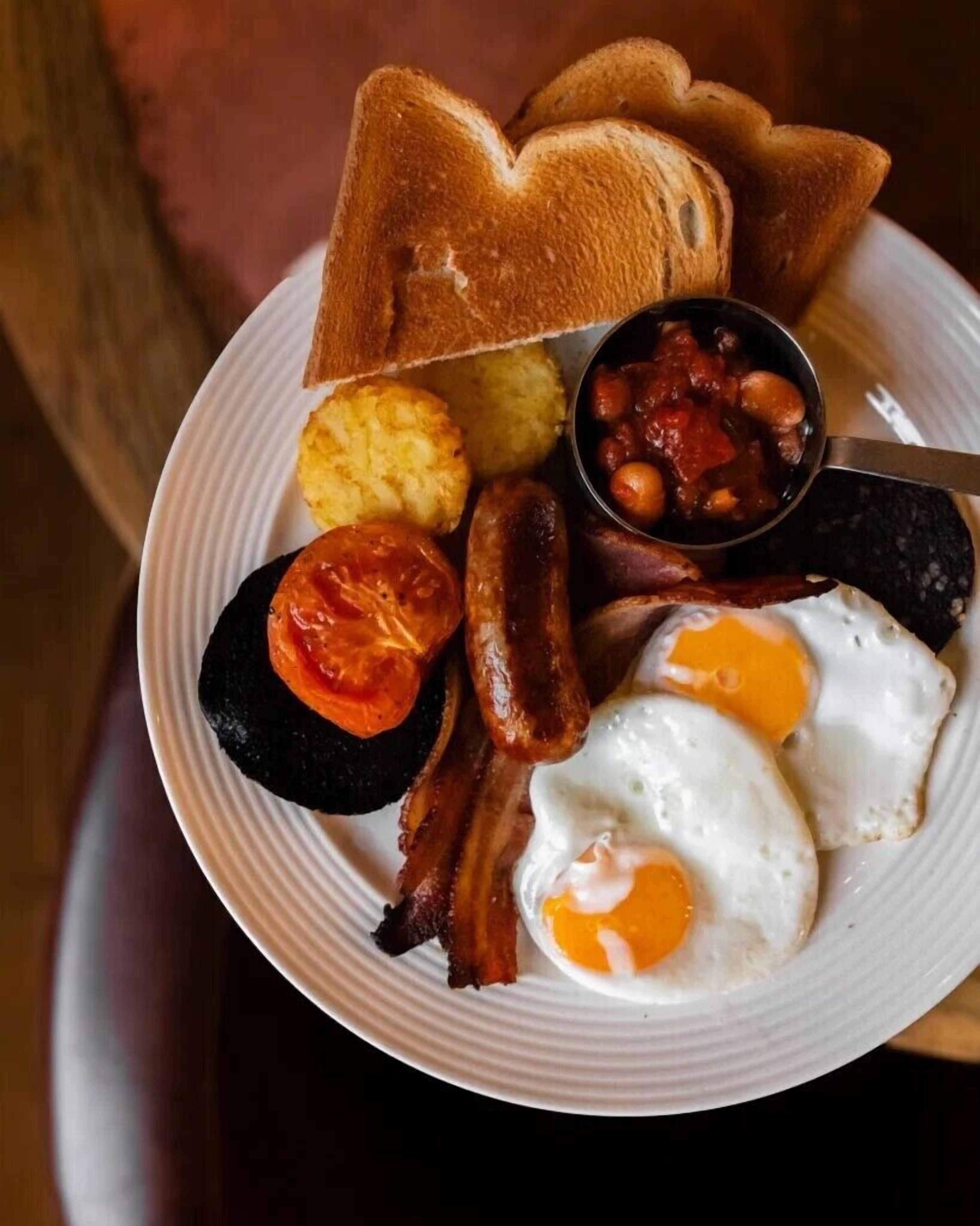 Un plato de desayuno con tostadas, frijoles, salchichas, huevos y tomates.