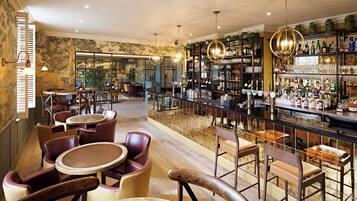 Zona de bar con sillas de madera, barra y estantes llenos de botellas.