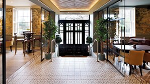 A spacious lobby with a patterned floor, a central seating area, and a view through a glass door to another room.