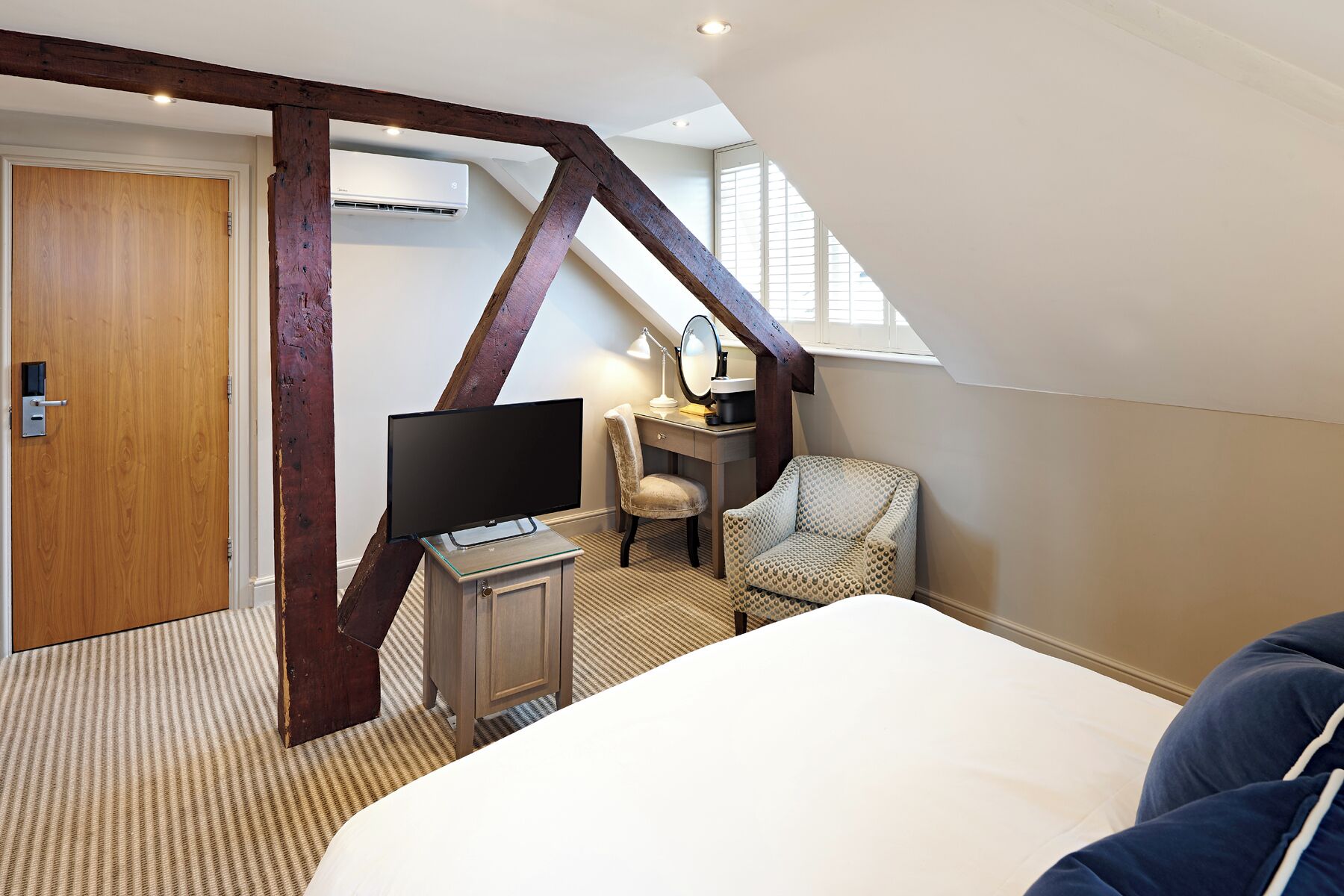 Un dormitorio con cama, escritorio con televisor, una silla y ventana.
