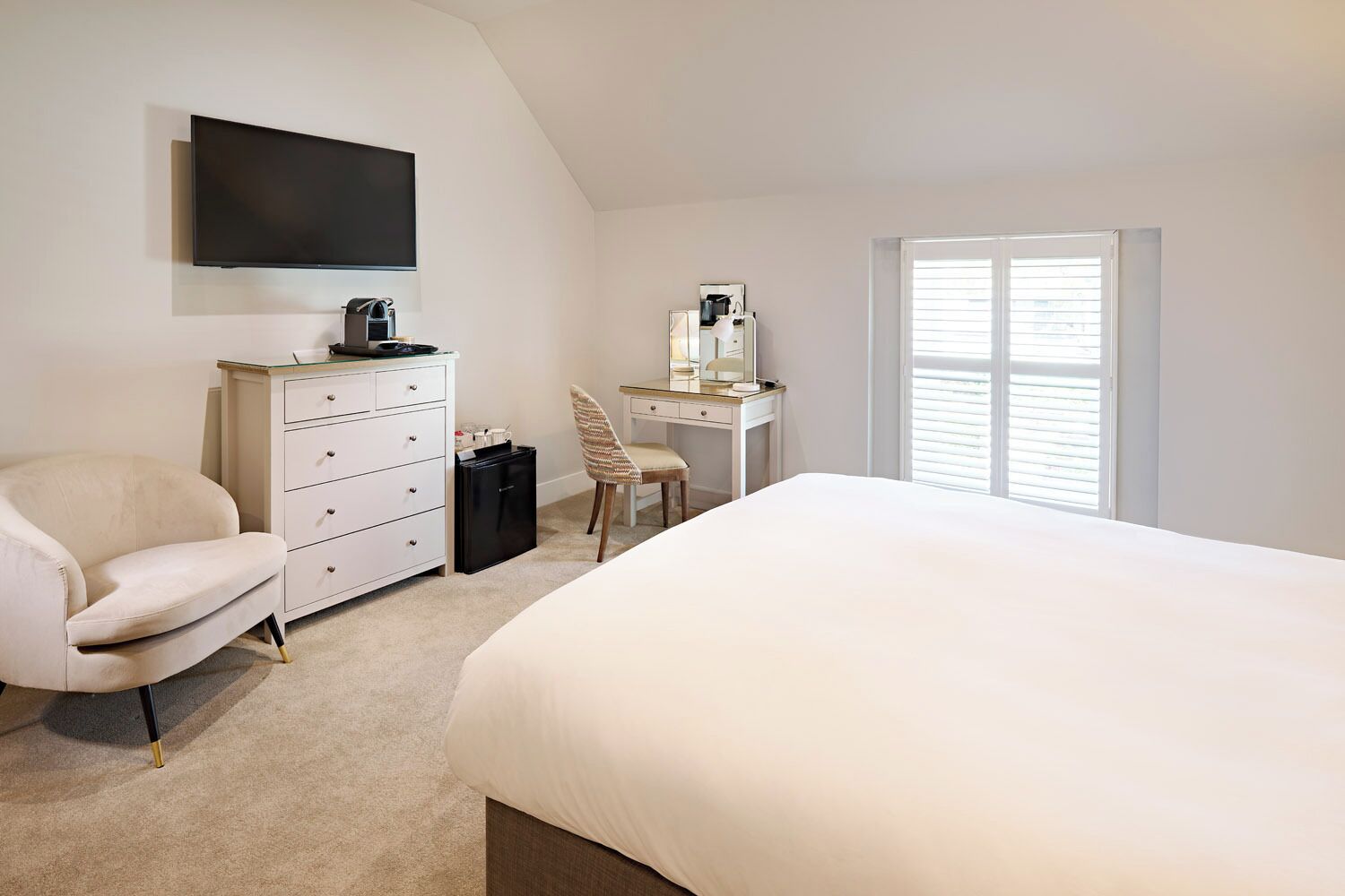 A bedroom with a bed, a desk, a chair, a dresser, a television, and a window.