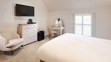 A bedroom with a bed, a desk, a chair, a dresser, a television, and a window.