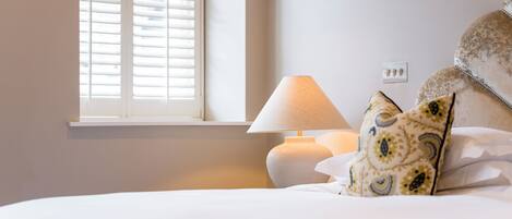 A bedroom with a bed, a bedside lamp, a window with blinds, and a pillow with a pattern.
