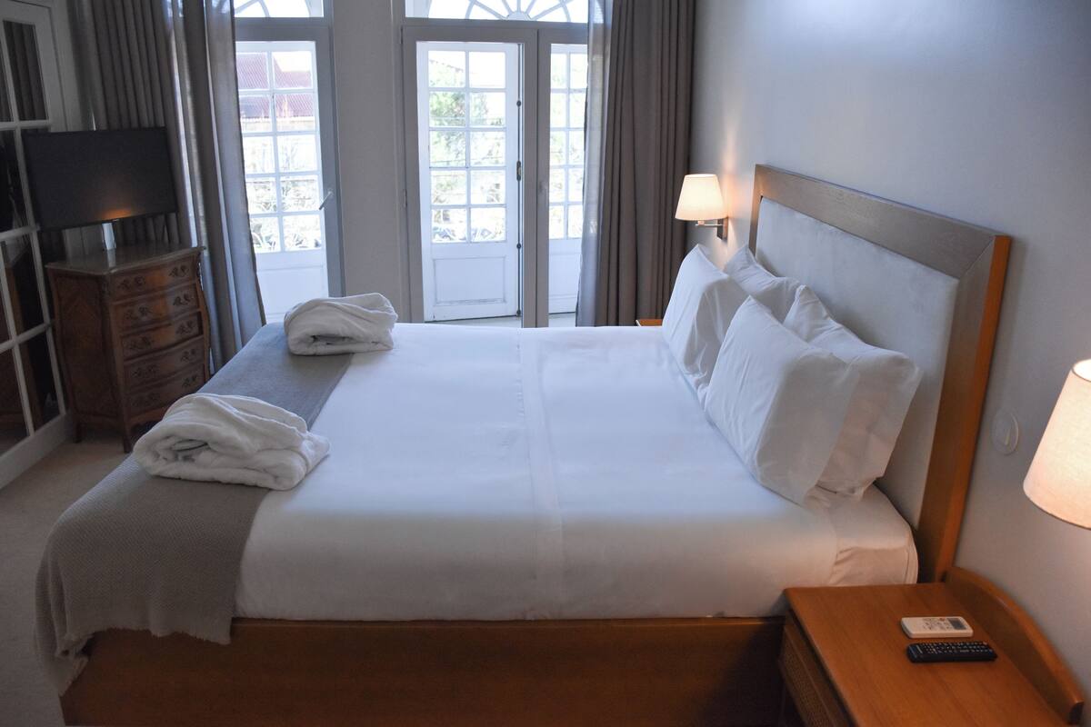 A neatly made bed with white linens and pillows, a wooden nightstand with a remote control, and a television on a dresser.