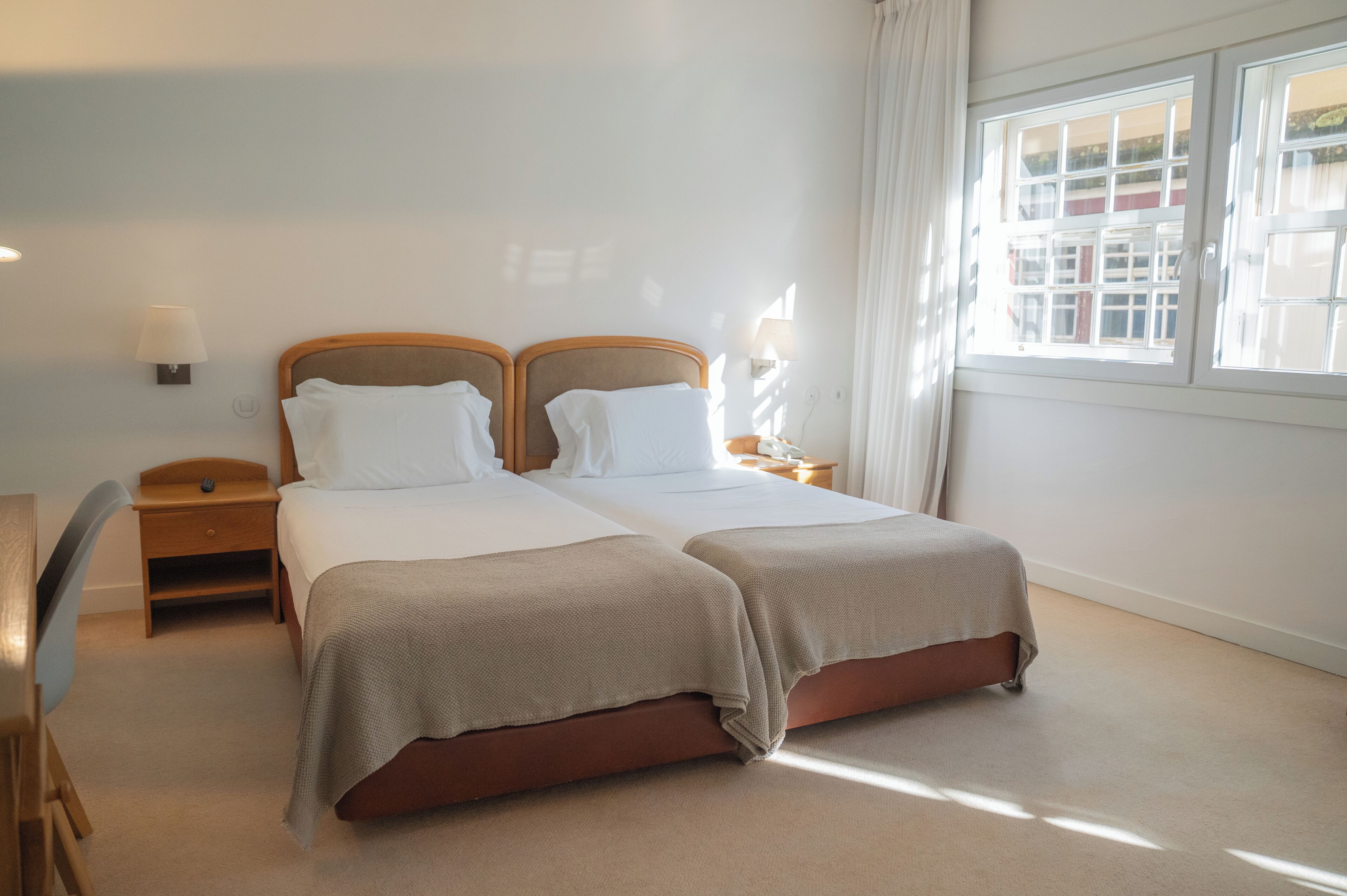 A hotel room with two beds, a desk, and a window with curtains.