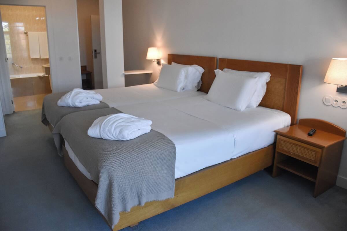 A hotel room with a large bed, two bedside tables, a nightstand, and a bathroom visible through an open door.
