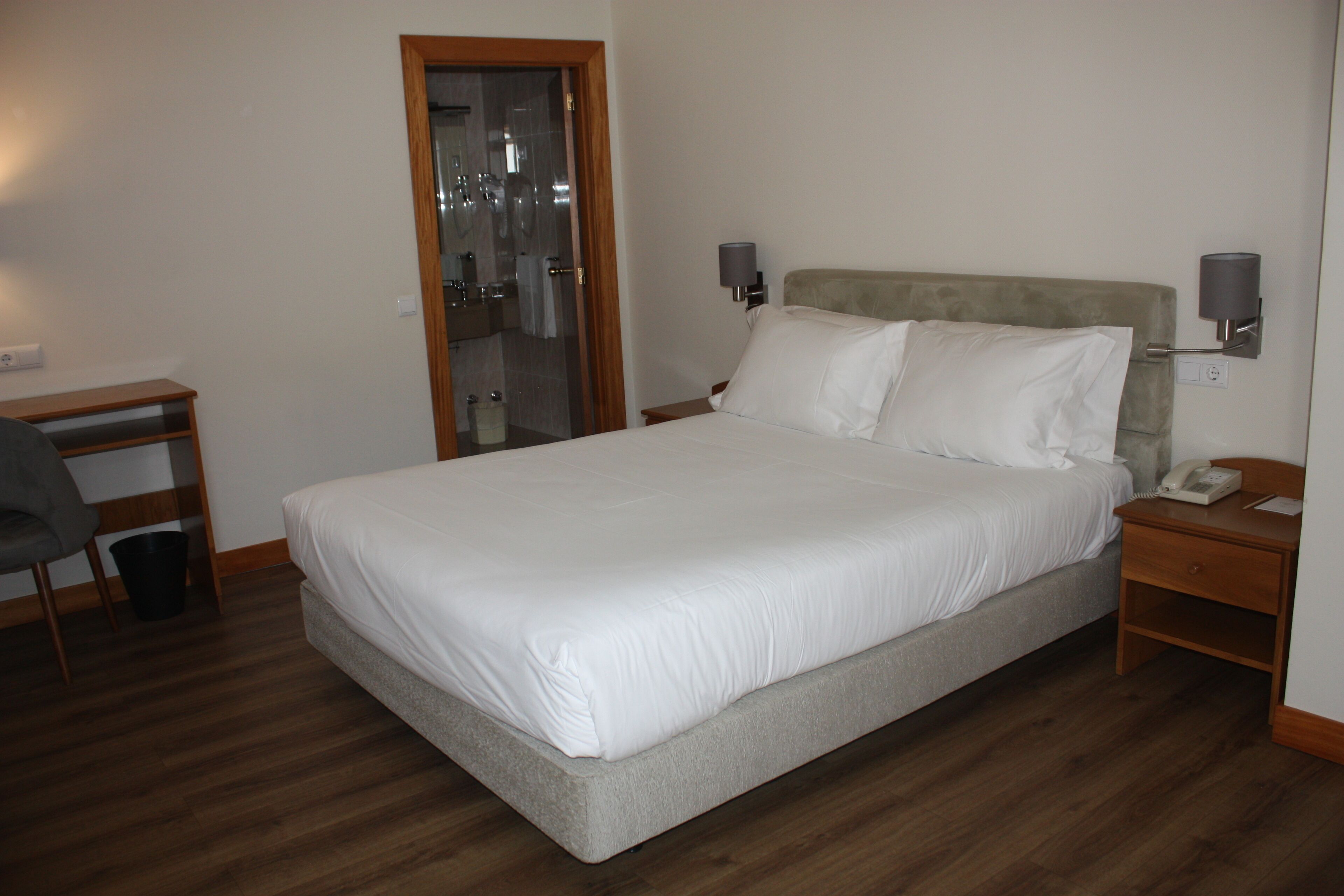 A hotel room with a bed, bedside tables, a desk, and a mirror.