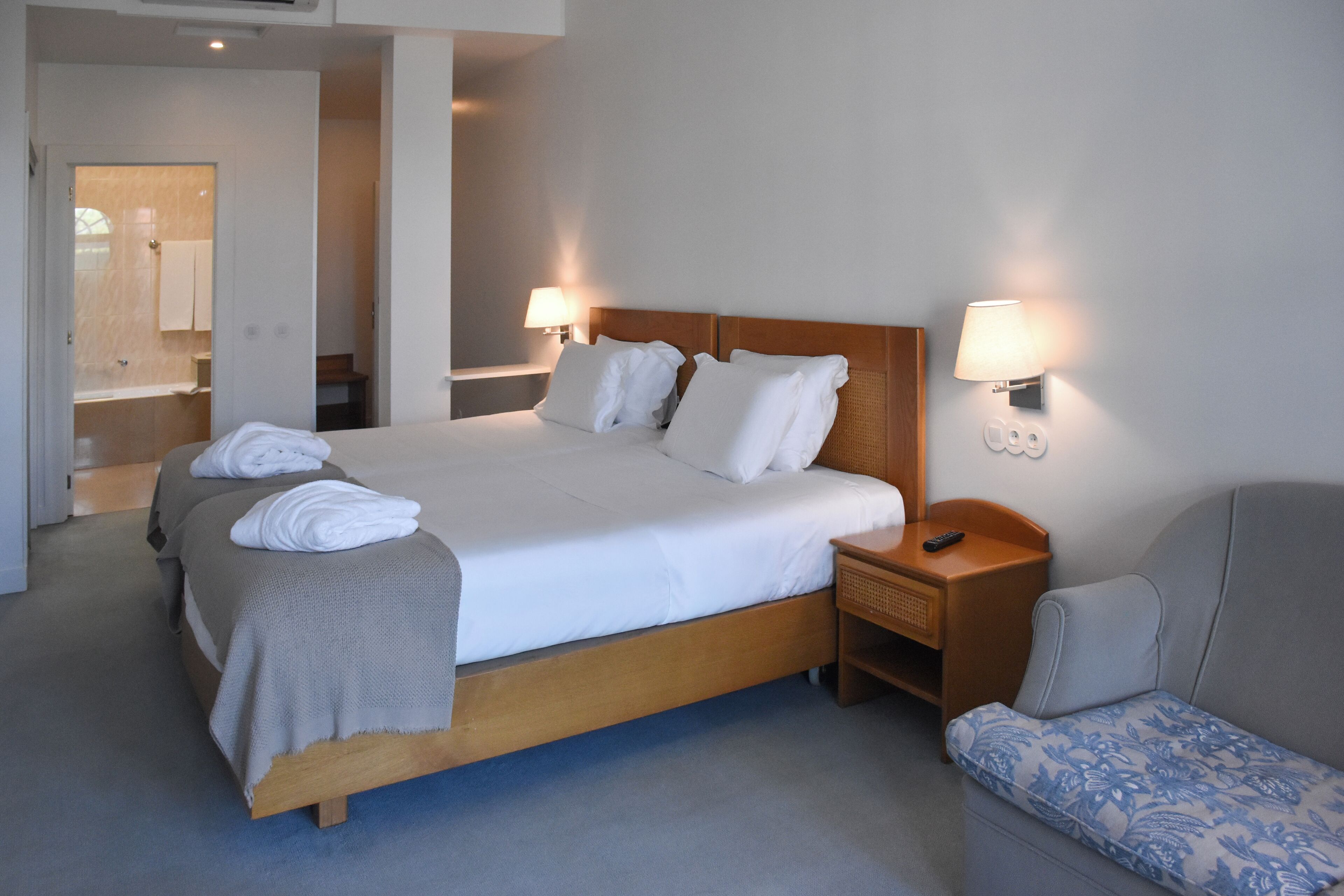 Et hotelværelse med en stor seng, to sengeborde med lamper, en sofa og et badeværelse, der kan ses gennem en åben dør.