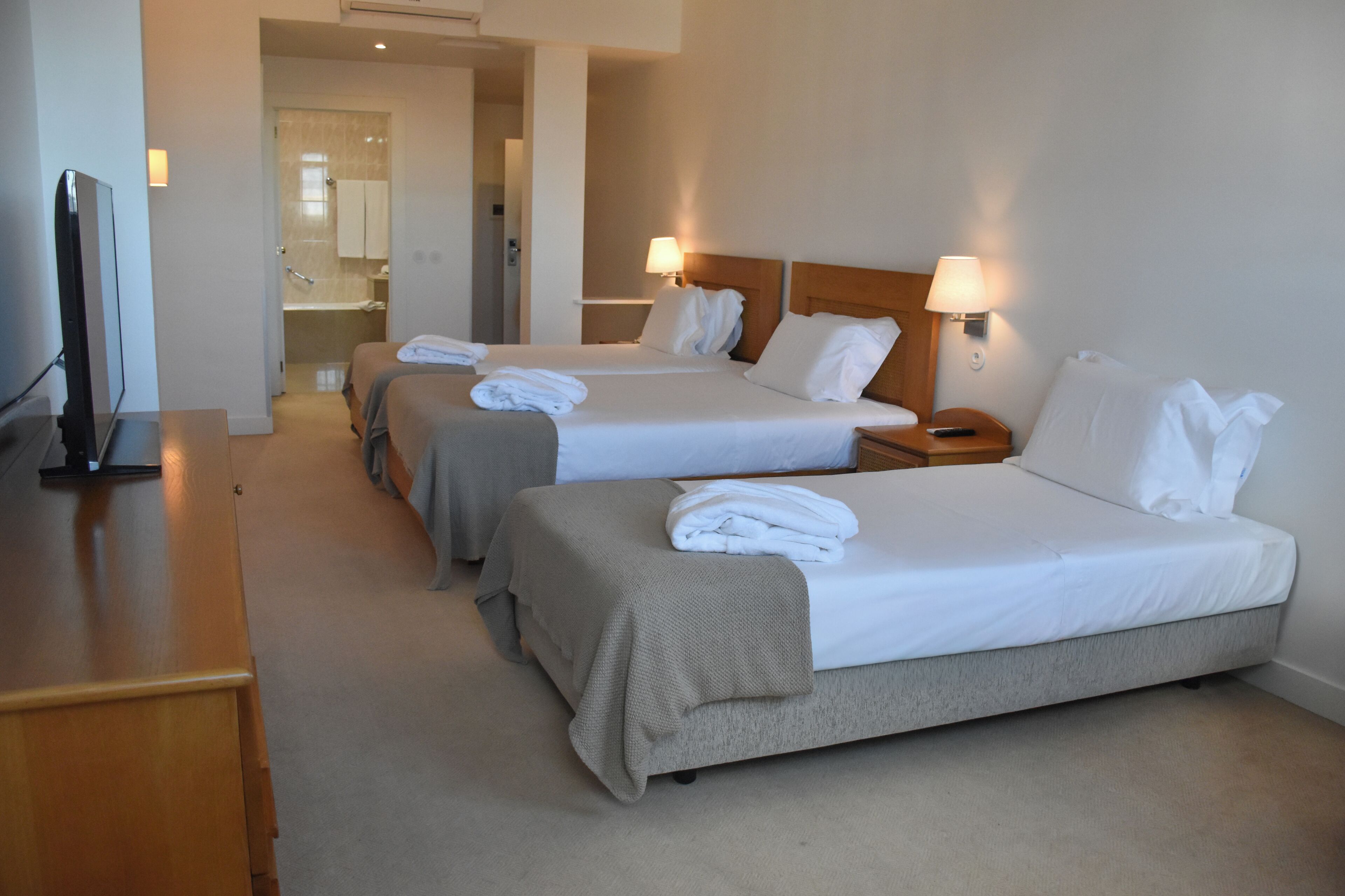Une chambre d’hôtel avec deux lits, une télévision, un bureau et une salle de bain visible à travers une porte ouverte.