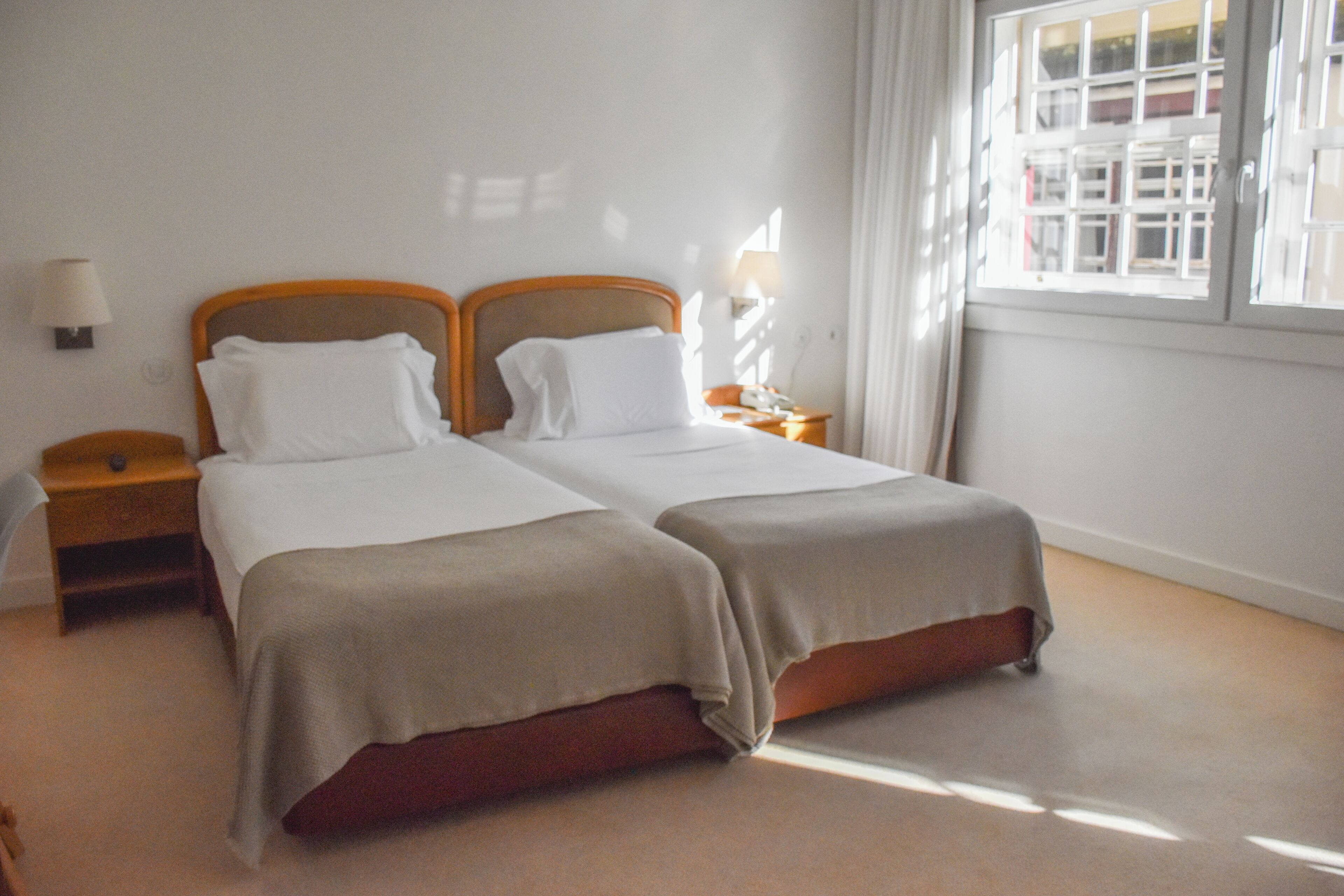 Una cama doble con cabecera de madera, una mesita de noche con lámpara y una ventana con cortinas.