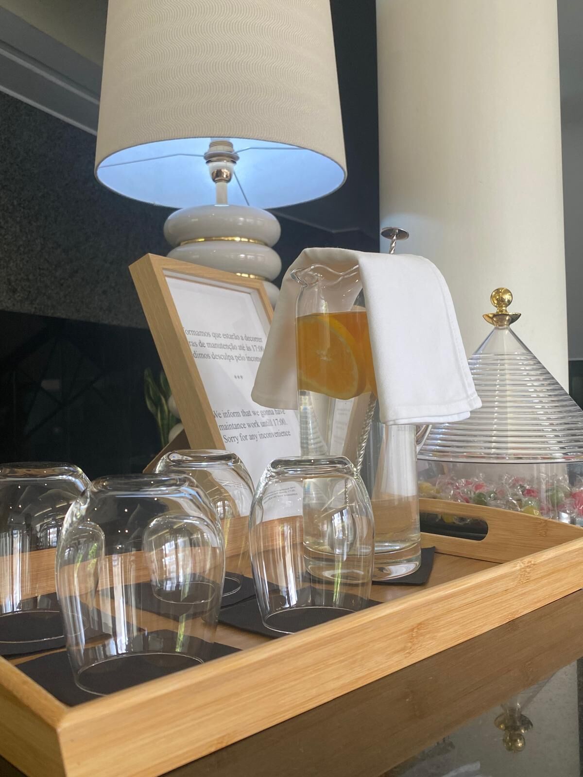 A tray with several clear glass tumblers, a white lamp, a glass carafe, and a framed sign.