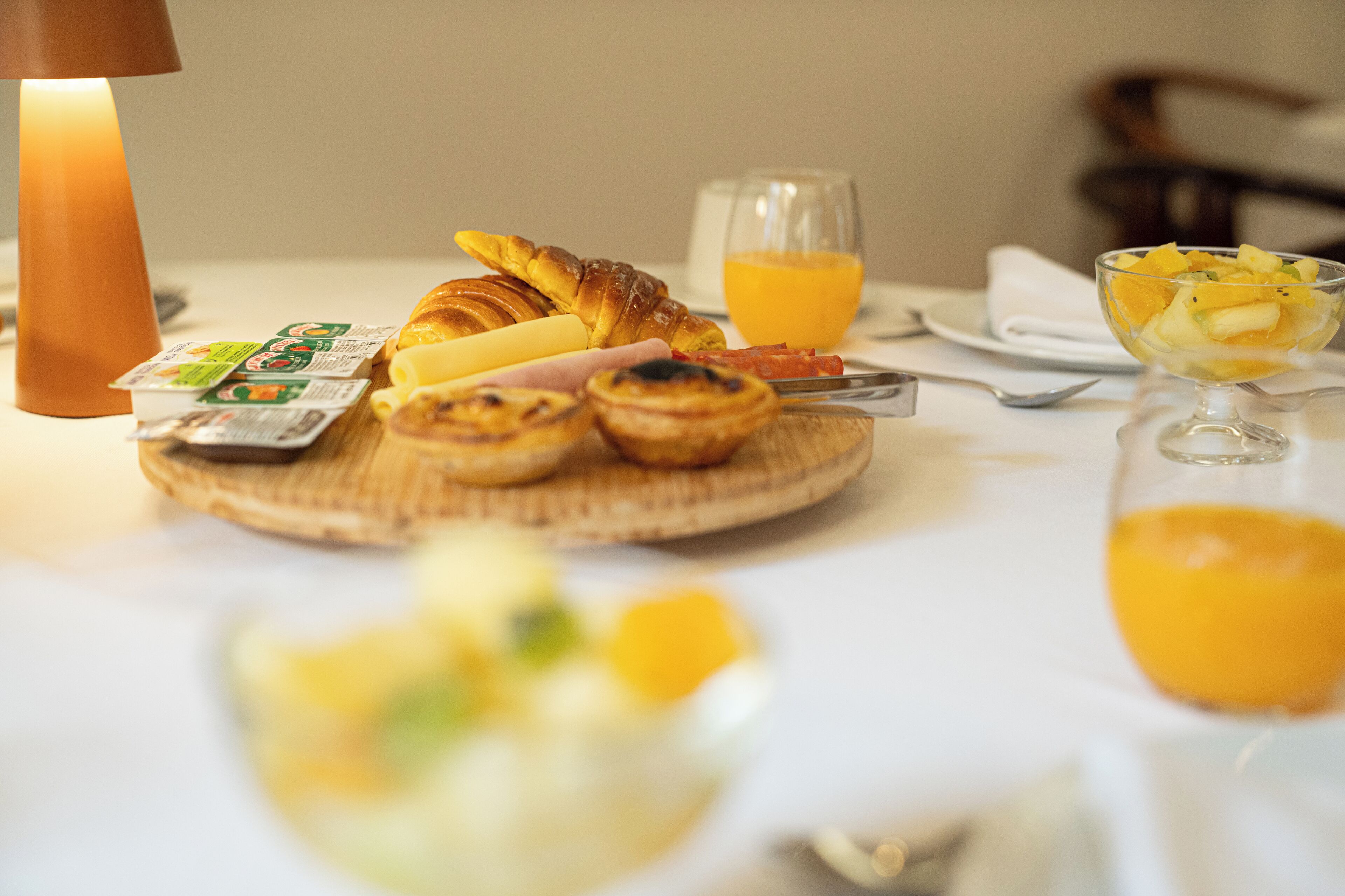 A breakfast setting with croissants, a glass of orange juice, and a bowl of fruit on a table.