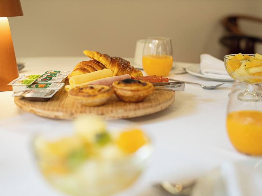 A breakfast setting with croissants, a glass of orange juice, and a bowl of fruit on a table.