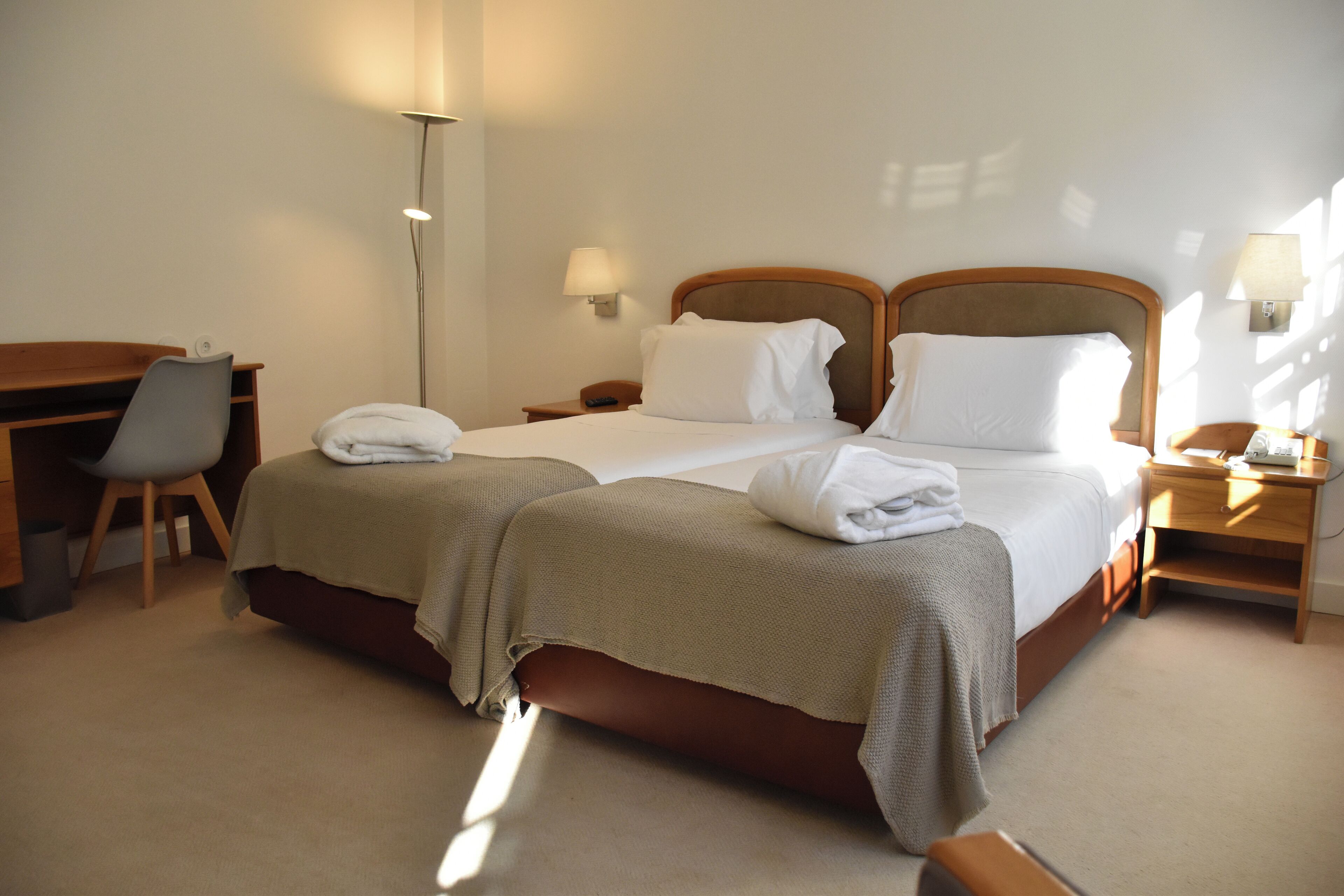 A hotel room with a double bed, two bedside tables, a desk with a chair, and a floor lamp.