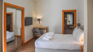 A hotel room with a bed, a desk, a chair, a TV, and a mirror.