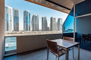A balcony with a view of modern skyscrapers, a wooden table, and two chairs.