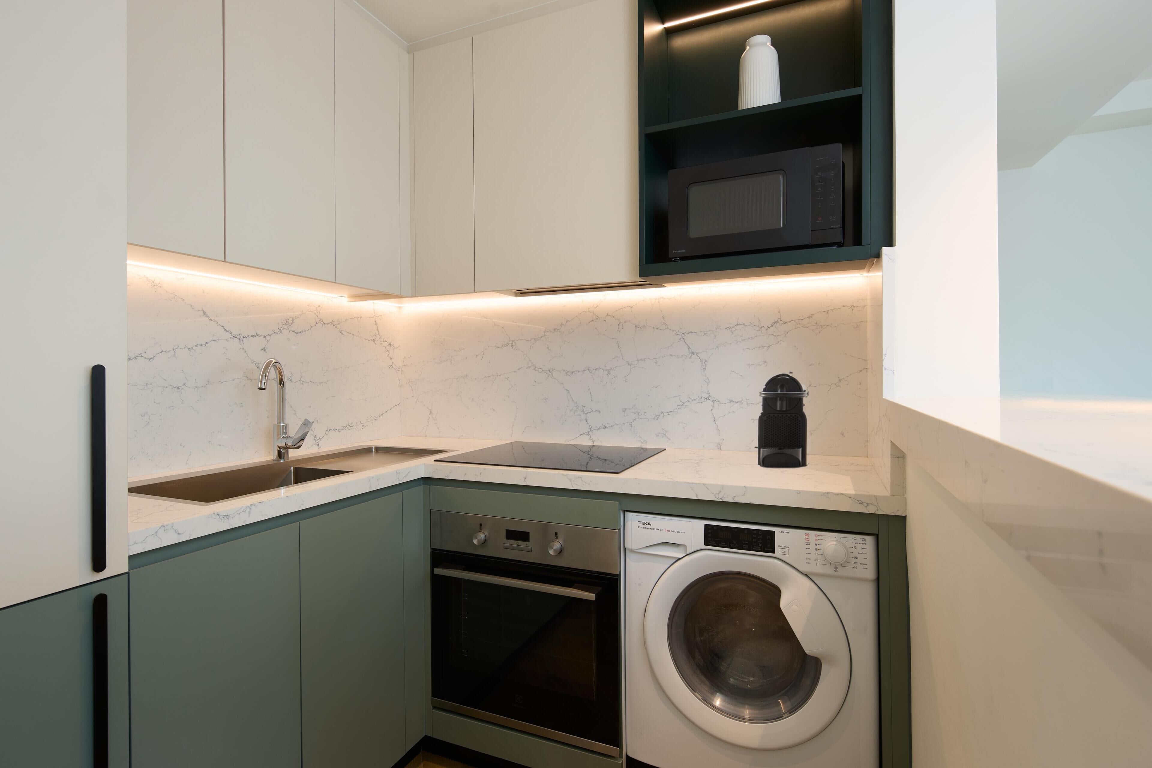 Een compacte keuken met een ingebouwde oven, magnetron en wasmachine.