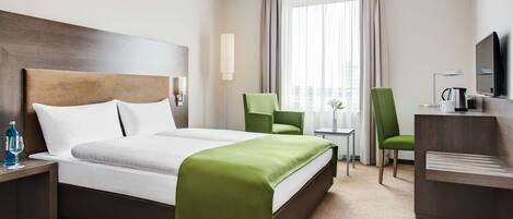 Una habitación de hotel con una cama grande, dos sillones, un escritorio, un televisor y una ventana con cortinas.