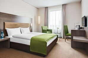 Et hotelværelse med en stor seng, to stole, et skrivebord, et fjernsyn og et vindue med gardiner.